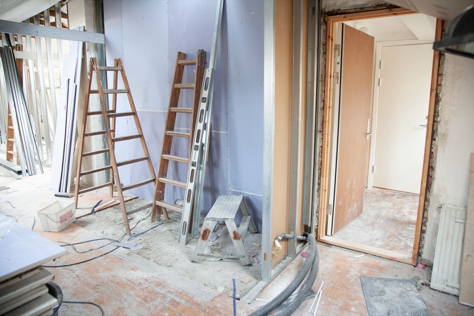 A room stripped back to boards and studwork mid-refurbishment, with ladders, a spirit level and new pipe runs in place