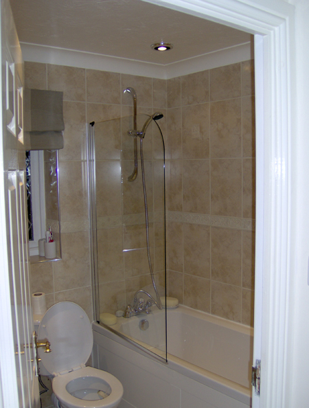 A family bathroom with a white bath, glass shower screen and stone-effect tiling taken to ceiling height over the bath