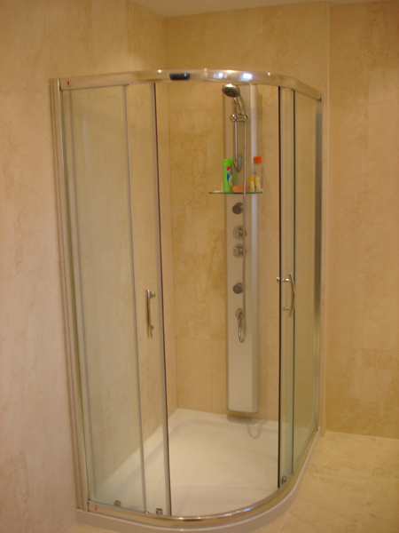 A curved quadrant shower enclosure with sliding glass doors and a chrome shower tower, in a warm stone-effect tiled bathroom