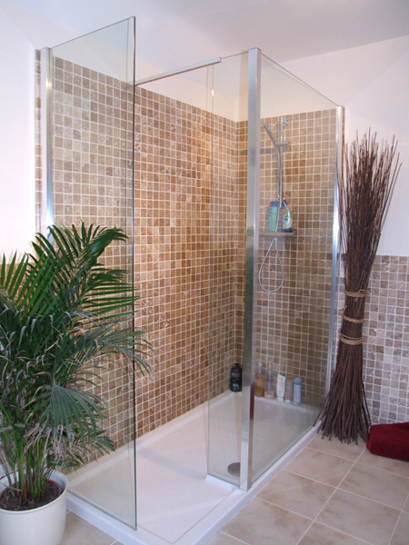 A walk-in shower tiled floor to ceiling in natural stone mosaic, with a low-level white tray and frameless glass screens